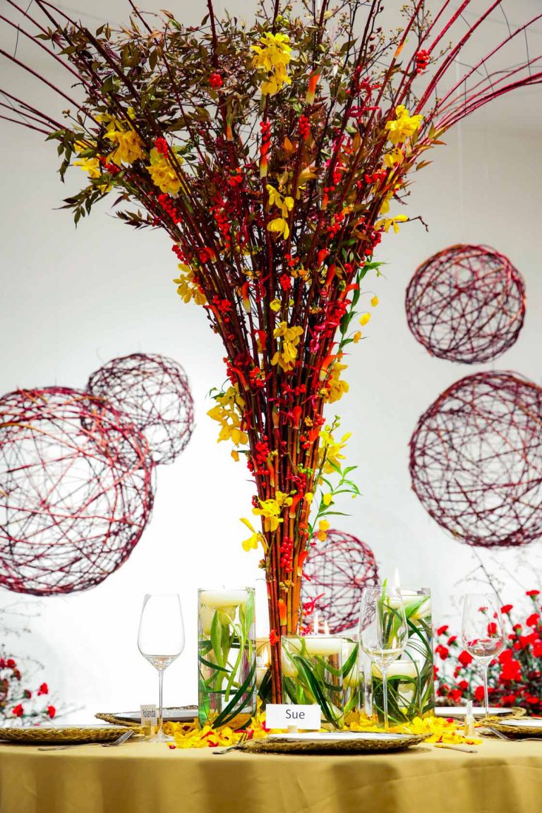 Conical table decoration created in Module 2 of the EFDE build from cornus branches, yellow and red orchids. In the background big red cornus balls.